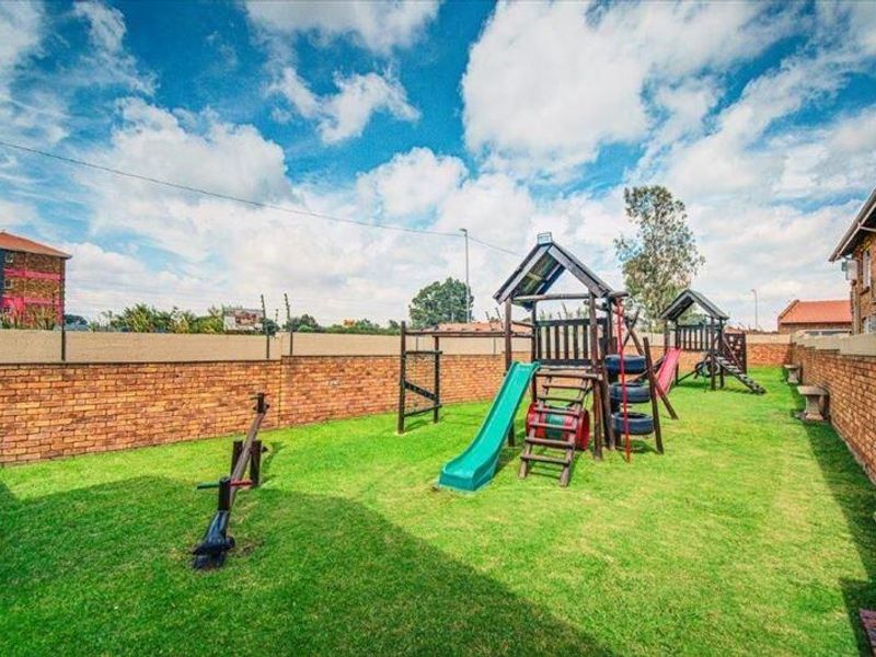 A communal garden area featuring a well-maintained lawn, brick boundary walls, and fixed playground equipment for residents.