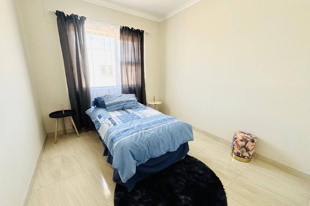 A bright bedroom featuring neutral tiled flooring and a window with curtain tracks.