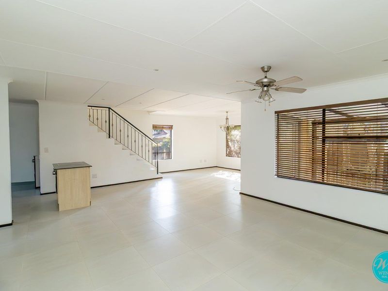 Spacious open-plan living area featuring neutral tiled flooring, a ceiling fan, and a staircase with a decorative metal railing.