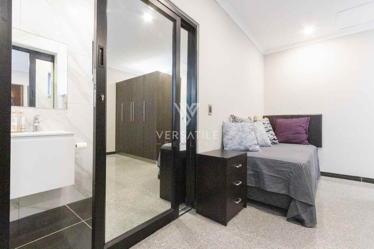 A modern bedroom featuring built-in wardrobes and an integrated en-suite bathroom with a vanity and tiled flooring.