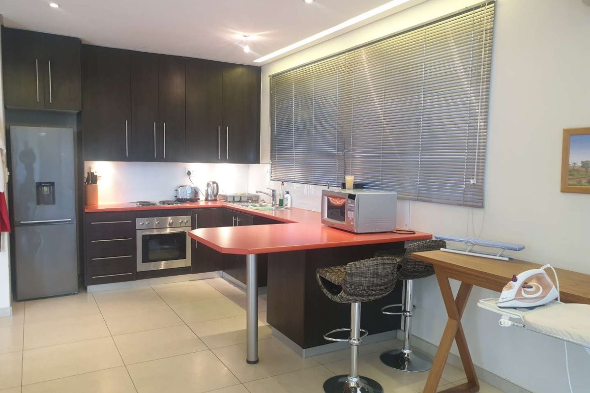 A functional kitchen featuring dark wood cabinetry, a contrasting red countertop, integrated oven and hob, and tiled flooring with recessed lighting.