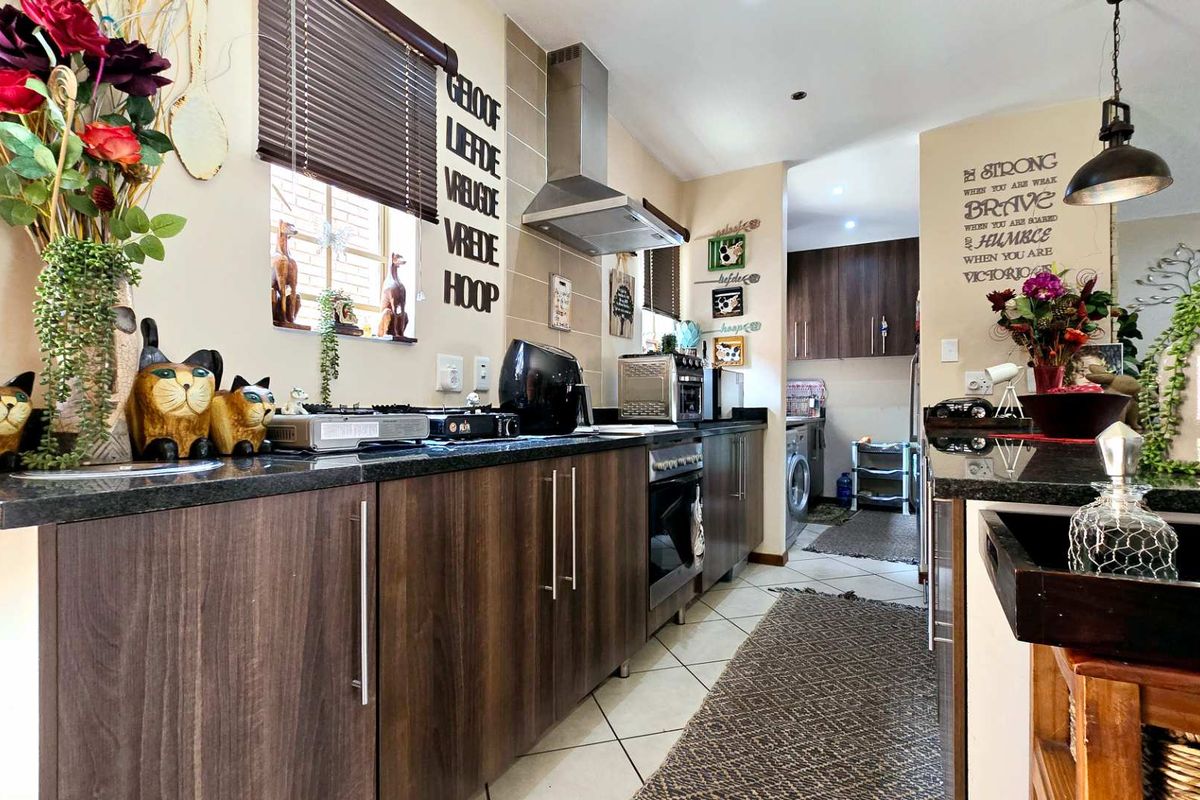 A functional kitchen featuring dark wood cabinetry, granite countertops, a stainless steel extractor fan, and a built-in oven, with an adjacent scullery area.