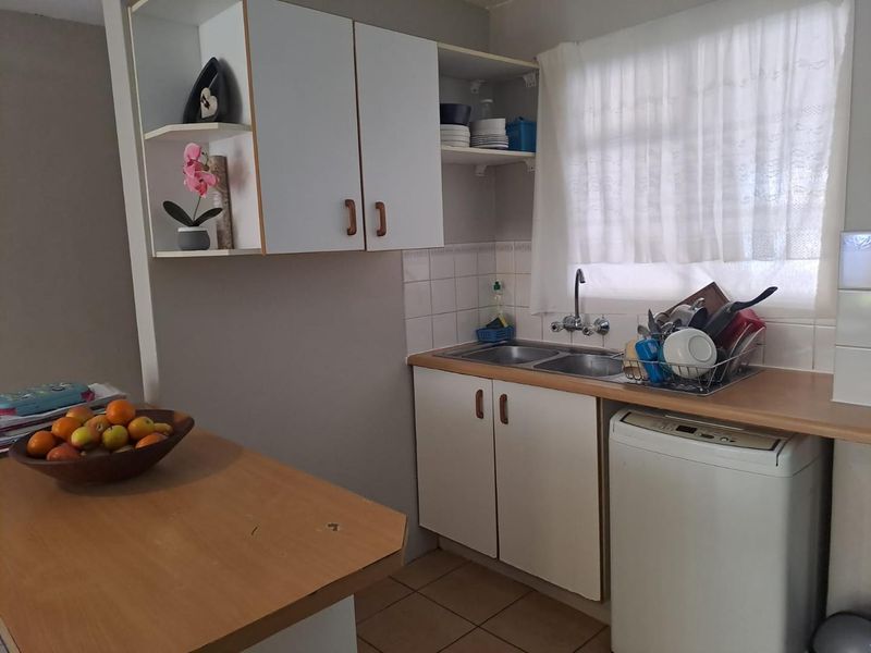 A functional kitchen featuring laminate countertops, a double bowl sink, and white cabinetry with tiled splashbacks and ceramic floor tiles.