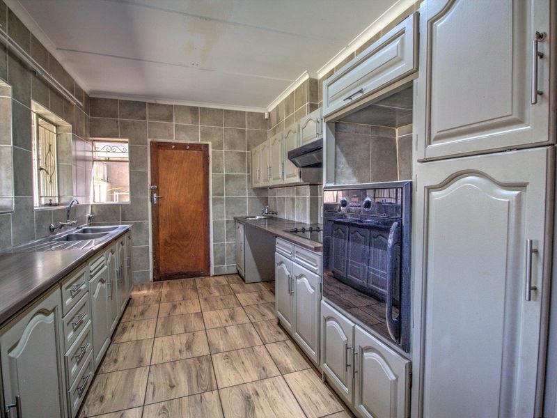 A functional kitchen featuring built-in cabinetry, a double sink, integrated oven and hob, with tiled flooring and wall finishes throughout.