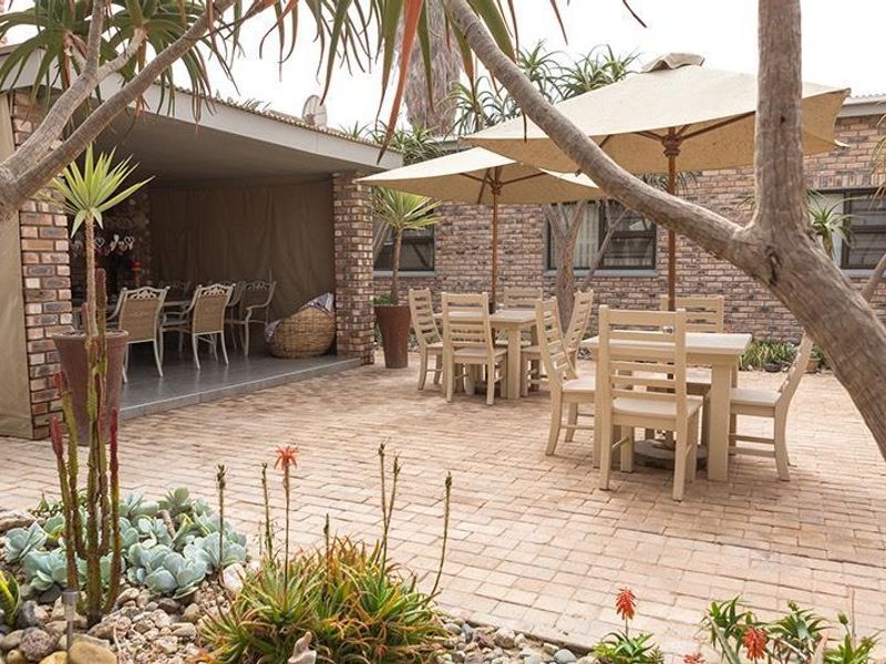 A spacious outdoor patio area featuring brick paving, a covered section, and established garden landscaping, ideal for outdoor dining and entertainment.