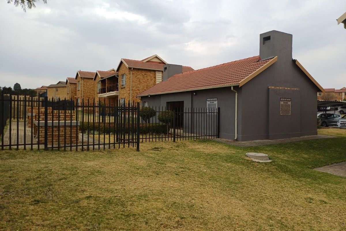 Exterior view of the apartment complex grounds featuring a communal brick braai area, manicured lawn, and secure perimeter fencing.