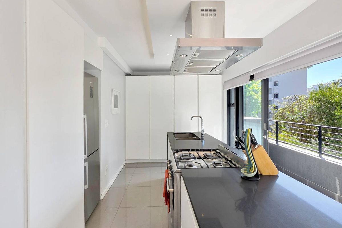 Modern kitchen featuring sleek white cabinetry, dark stone countertops, a gas hob, stainless steel extractor fan, and direct access to a balcony.