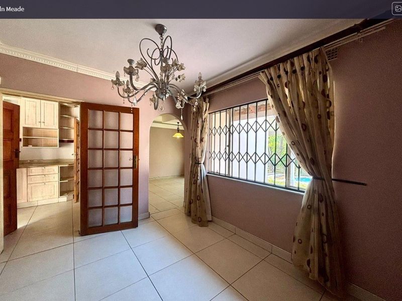 A vacant living area featuring tiled floors, an ornate ceiling cornice, and an archway leading to adjacent spaces, with a security-fitted window.