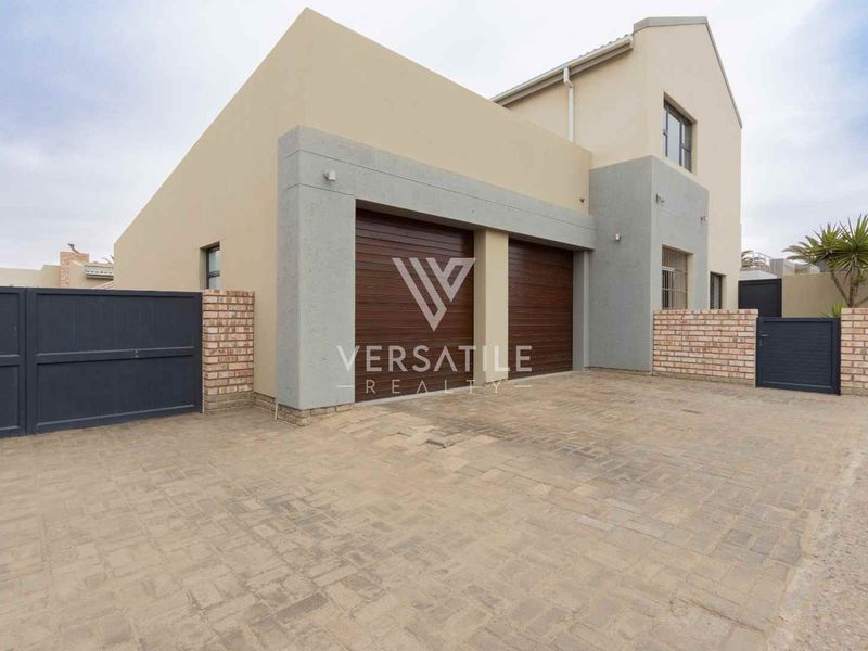 Modern double-storey home exterior featuring a paved driveway, double garage with sectional doors, and secure boundary walling.