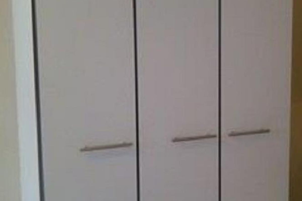 A simple white built-in wardrobe with modern handles, providing functional storage space within the bedroom.