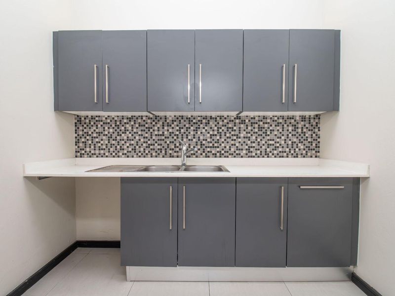 A clean and functional laundry area featuring modern grey cabinetry, a stainless steel sink, and a decorative mosaic tile backsplash.