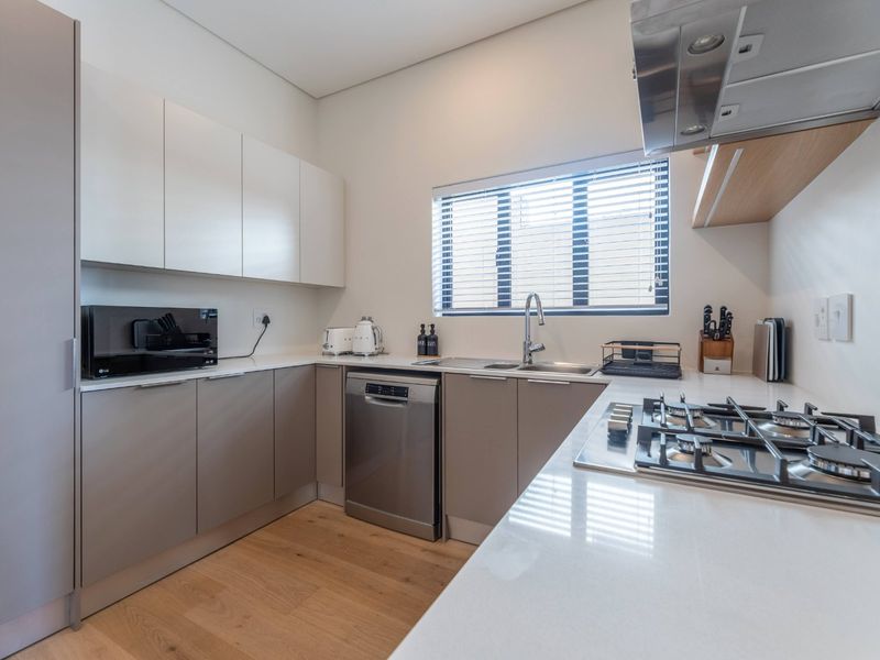 Modern kitchen featuring sleek cabinetry, stone countertops, a gas hob with extractor fan, and integrated dishwasher, finished with light wood-look flooring.