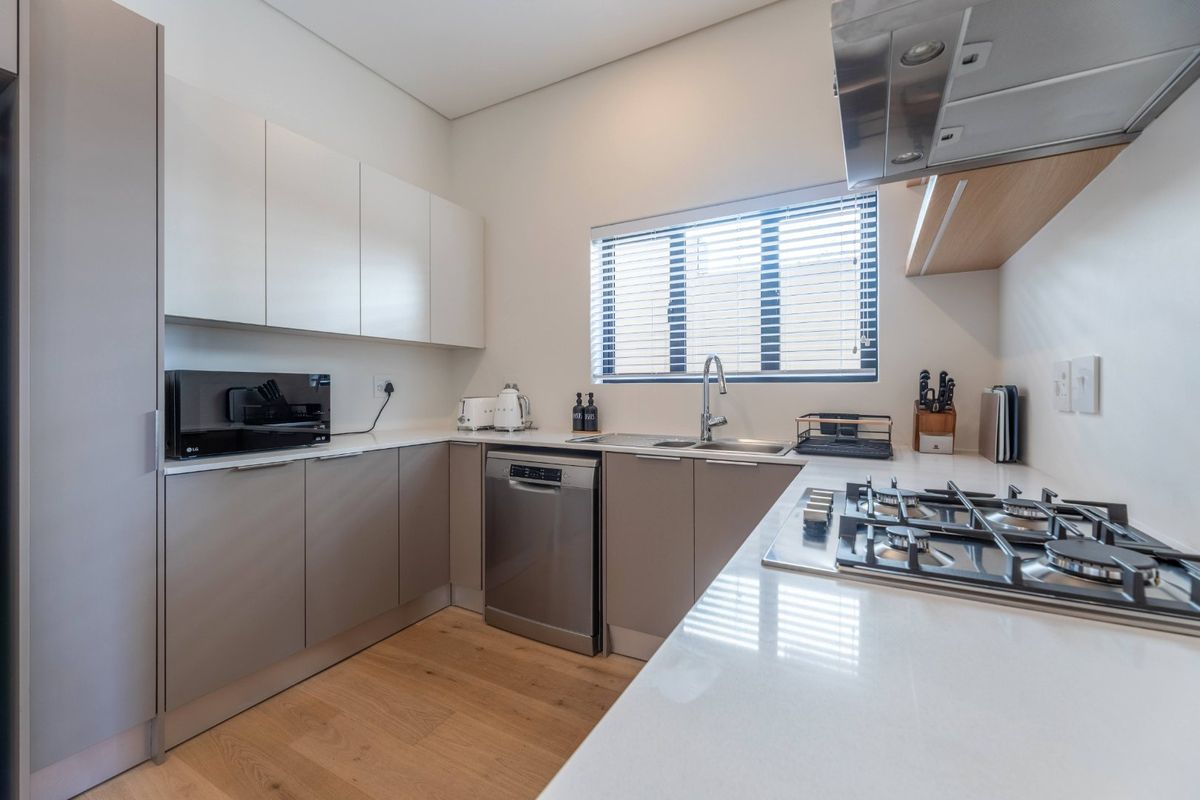 Modern kitchen featuring sleek cabinetry, stone countertops, a gas hob with extractor fan, and integrated dishwasher, finished with light wood-look flooring.