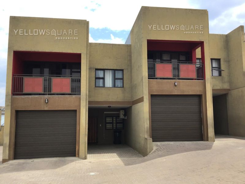 Front elevation of a modern townhouse complex featuring double garages, private balconies, and paved driveway access.