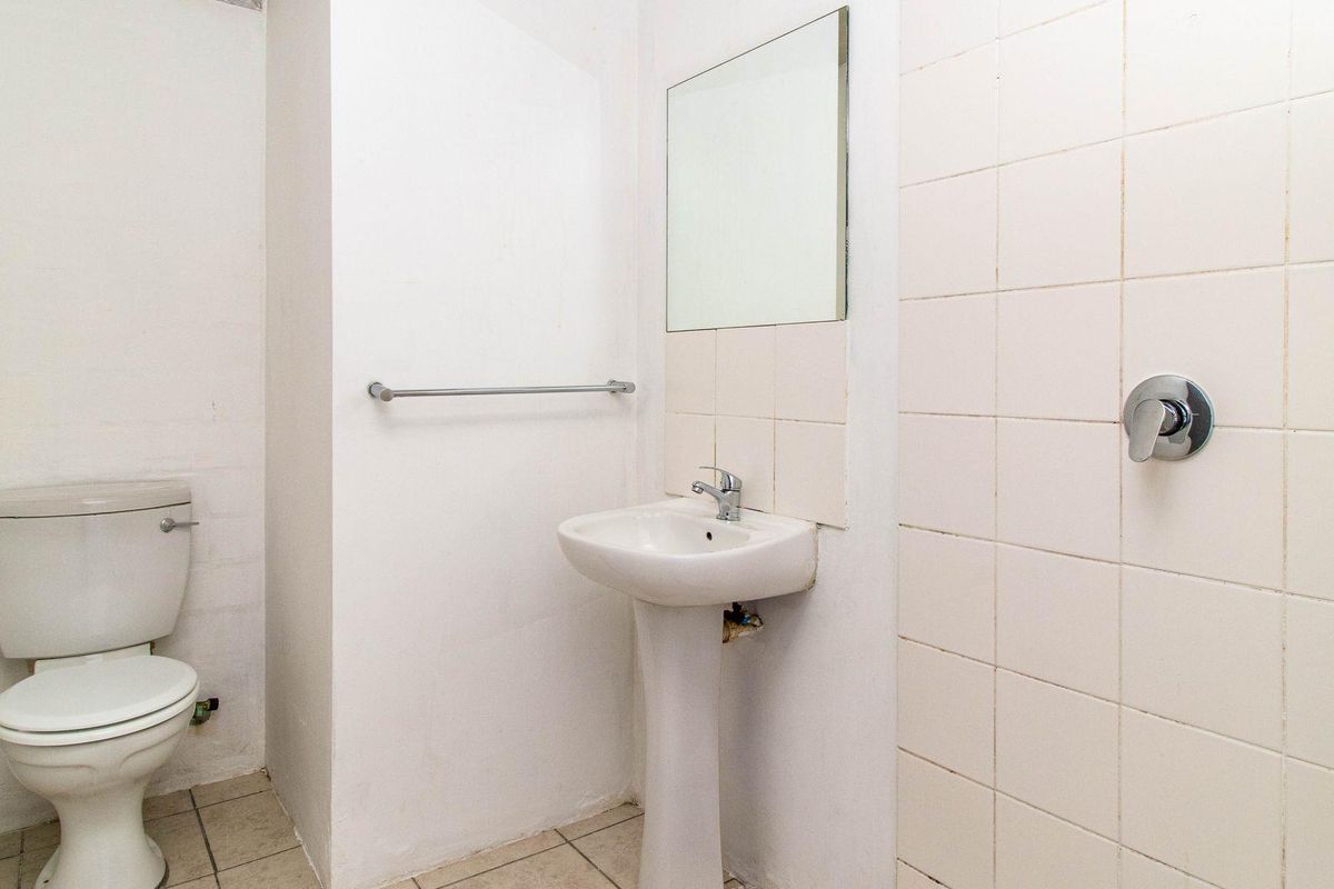 A functional bathroom featuring a pedestal sink, a standard toilet, and tiled shower area with wall-mounted fixtures.