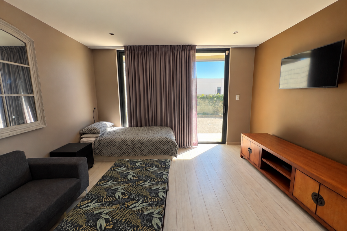 A well-lit bedroom featuring tiled flooring, recessed ceiling lighting, and a large sliding glass door providing direct access to the outdoor area.