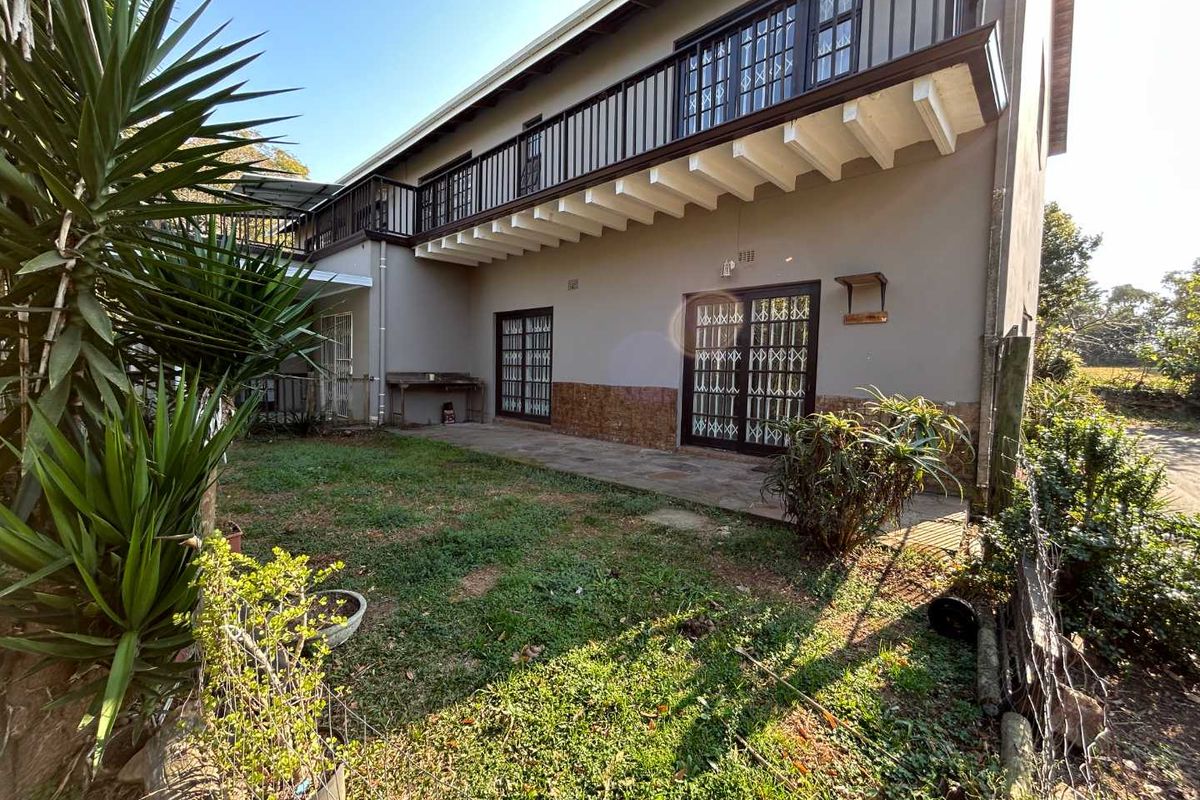 Rear exterior view of the cottage featuring a stone patio, security gates, and an upper-level balcony with metal railings.