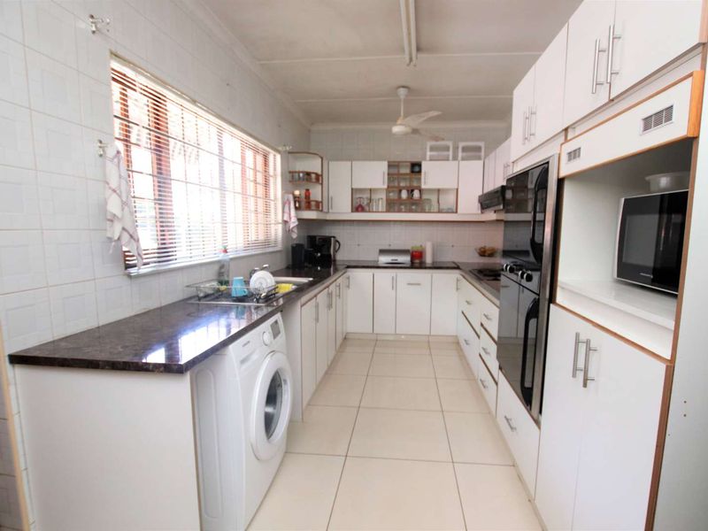 A functional kitchen featuring white built-in cabinetry, dark laminate countertops, tiled walls, and integrated appliances including an oven and microwave.
