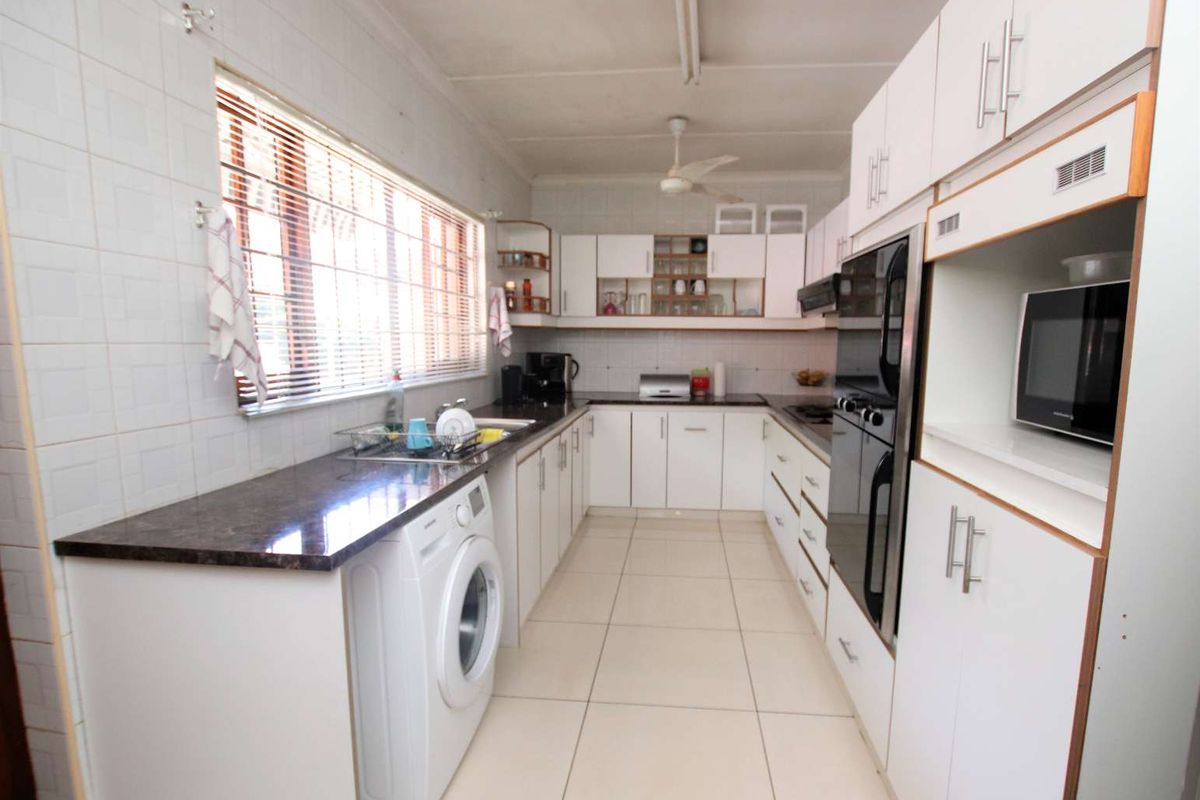 A functional kitchen featuring white built-in cabinetry, dark laminate countertops, tiled walls, and integrated appliances including an oven and microwave.