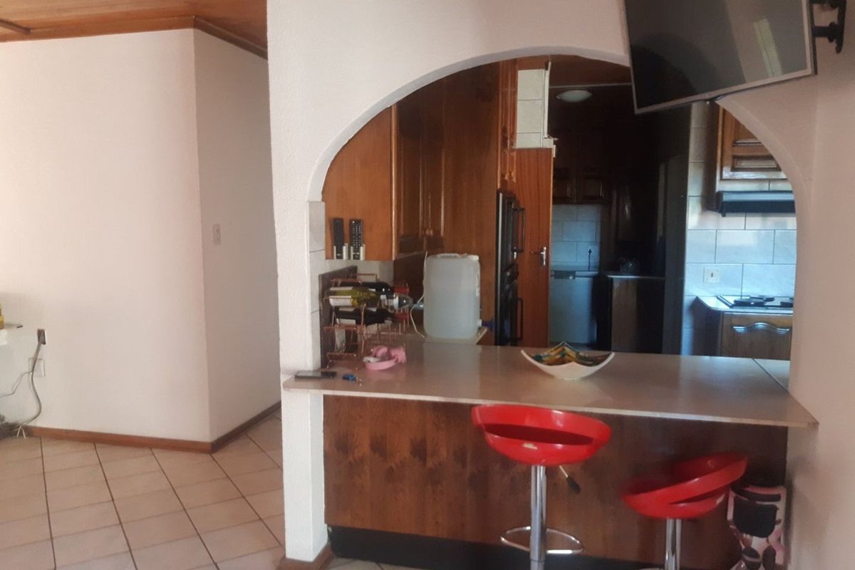 A dated kitchen featuring an arched opening, wooden cabinetry, and a breakfast bar, with tiled flooring throughout the space.