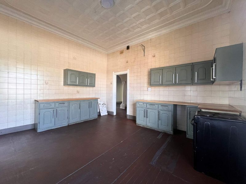 A spacious, empty kitchen featuring original pressed metal ceilings, tiled walls, and dated cabinetry, offering significant potential for a modern renovation.
