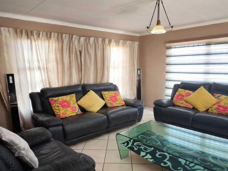A comfortable living room featuring tiled flooring, neutral wall tones, and window blinds, providing a functional and well-lit space for relaxation.