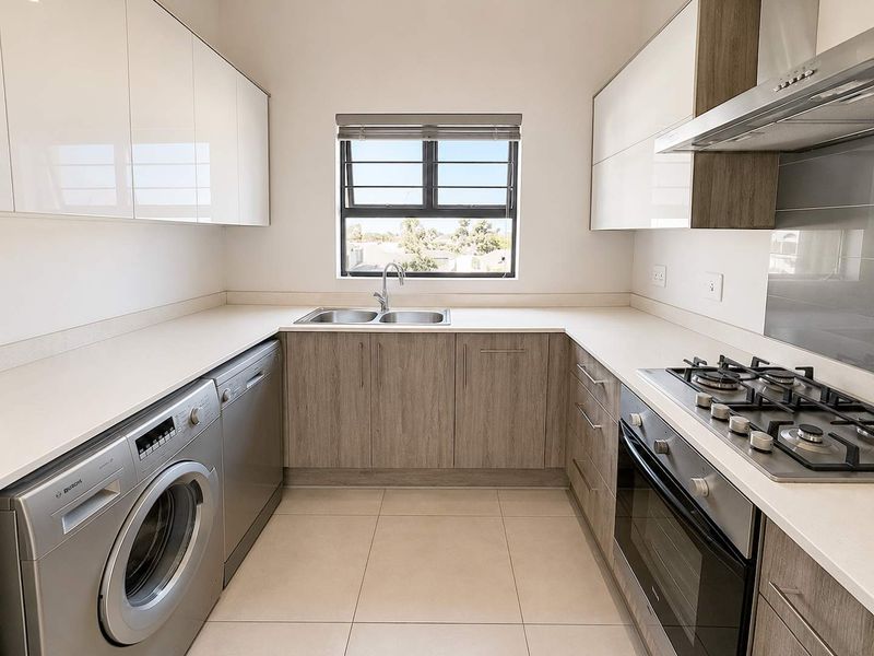 Modern kitchen featuring sleek white and wood-grain cabinetry, stone countertops, integrated gas hob, oven, extractor fan, and tiled flooring.