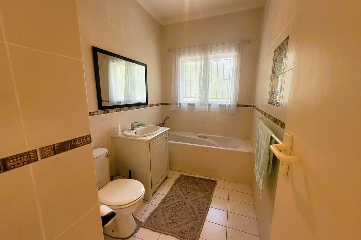 A functional bathroom featuring a built-in bathtub, a vanity basin, and a toilet, finished with neutral wall tiles and floor tiling.