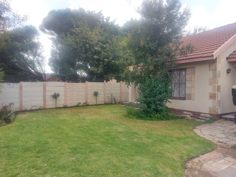 A rear garden view of the cottage featuring a lawn, paved pathway, and a precast concrete boundary wall.