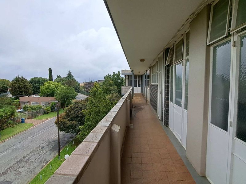 A long, open-air balcony featuring tiled flooring and a brick balustrade, providing access to the apartment through multiple glass doors.