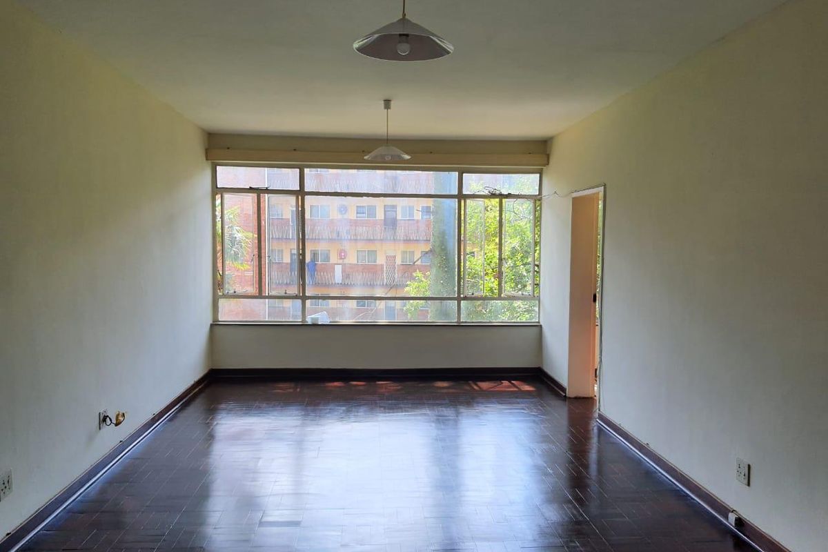 An empty living room featuring dark parquet flooring, large windows providing natural light, and simple pendant lighting, ready for personalization.