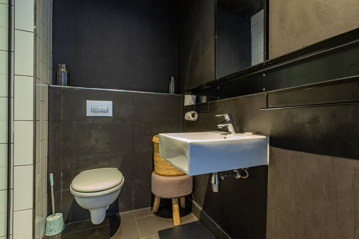 Modern bathroom featuring a wall-mounted basin, concealed cistern toilet, and dark tiled finishes, creating a contemporary and compact aesthetic.