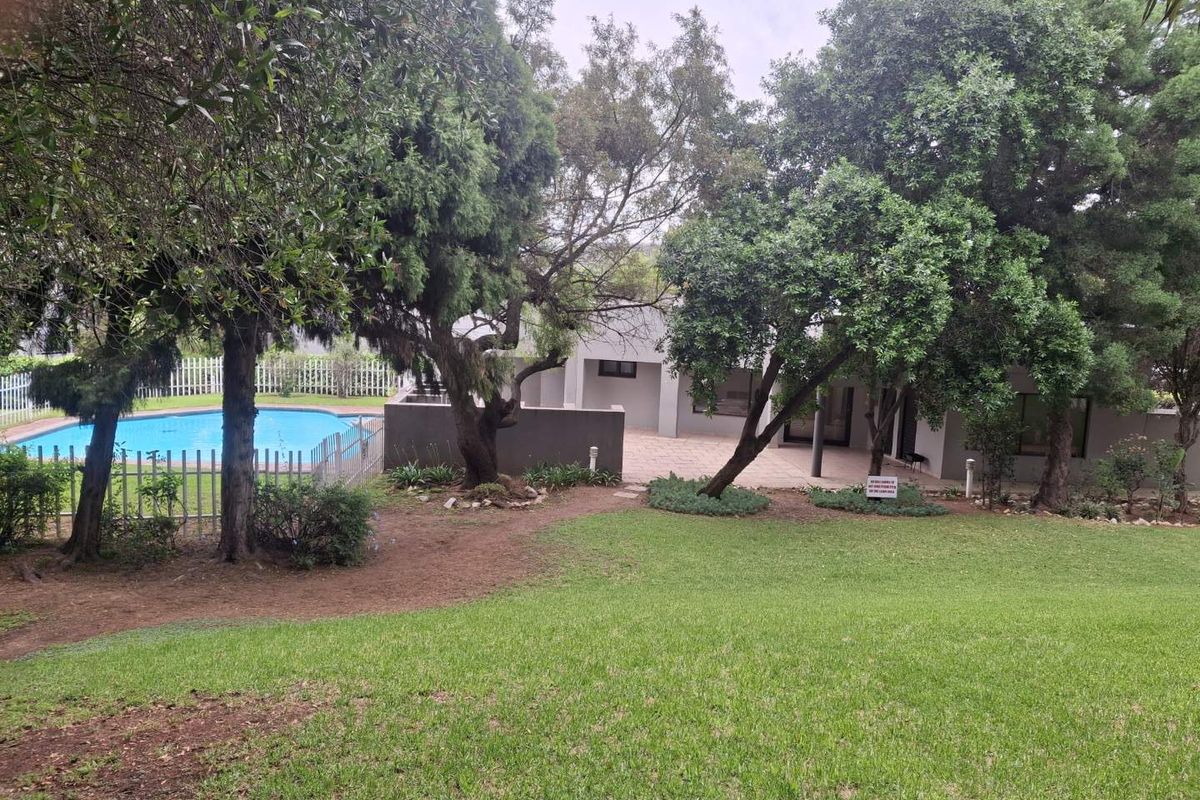 Rear garden view featuring a swimming pool, paved patio area, and established trees within a fenced property boundary.