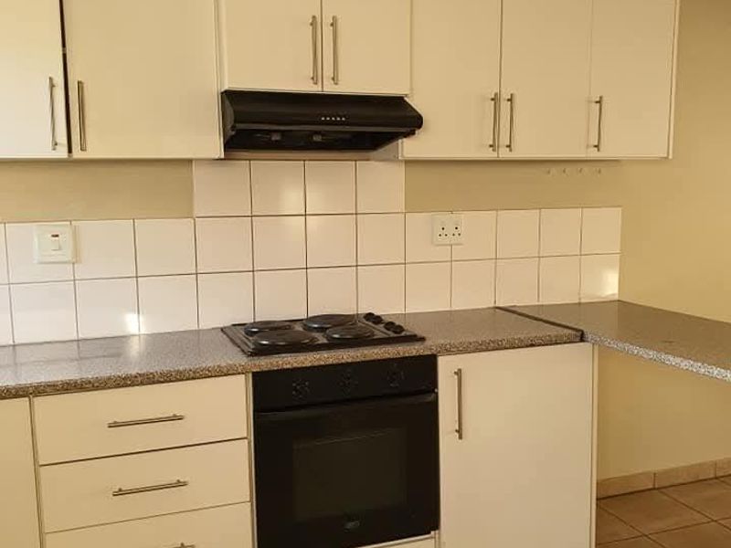 A functional kitchen featuring white cabinetry, laminate countertops, a built-in oven, electric hob, and a tiled backsplash.