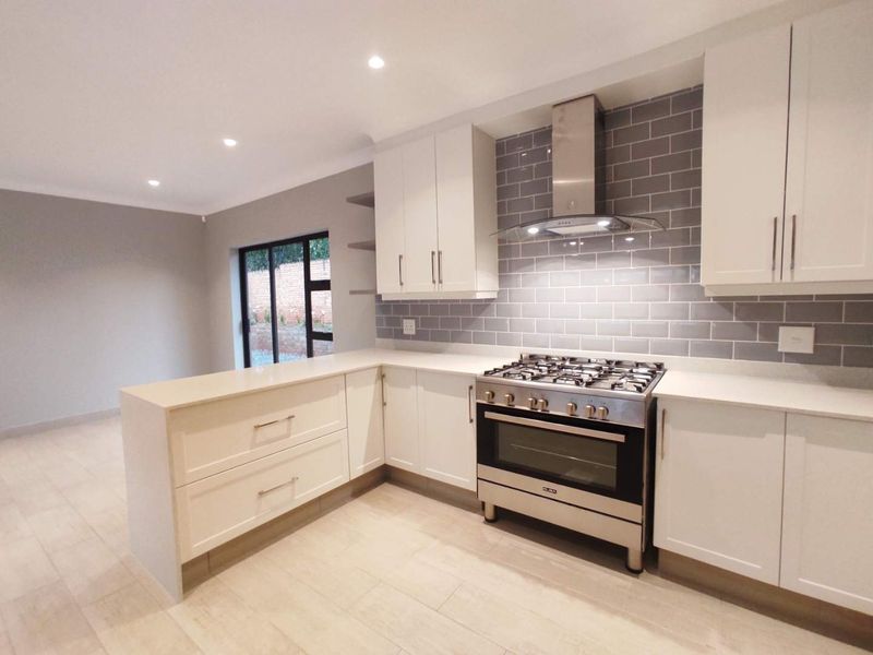 Modern kitchen featuring white cabinetry, quartz countertops, subway tile backsplash, and a stainless steel gas stove with an integrated extractor fan.