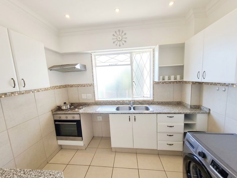 A functional kitchen featuring white cabinetry, granite countertops, a built-in oven with hob, extractor fan, and tiled finishes throughout.