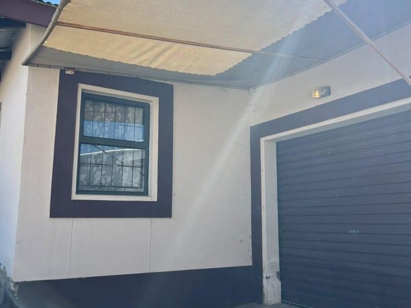 Front exterior view of the townhouse featuring a roller garage door, paved driveway, and a protective shade sail over the entrance area.