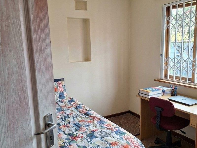 A compact bedroom featuring a ceiling fan, a built-in wall niche, and a window fitted with a security gate.