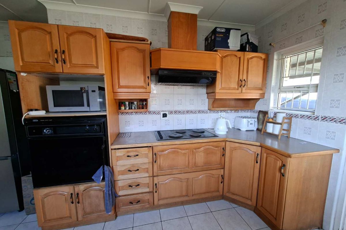 A functional kitchen featuring traditional wooden cabinetry, built-in oven, hob, extractor fan, and tiled splashbacks with neutral floor tiles.