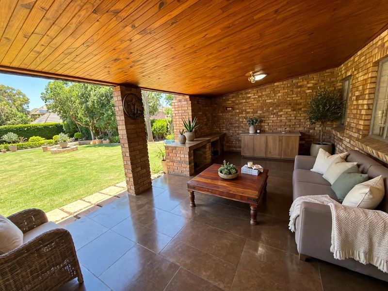 A spacious covered patio featuring exposed brick walls, a warm timber ceiling, and tiled flooring, overlooking a well-maintained garden.
