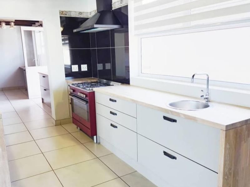 Modern kitchen featuring clean white cabinetry, wooden countertops, a gas stove with extractor fan, and tiled flooring with exposed ceiling beams.