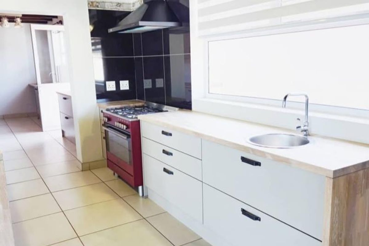 Modern kitchen featuring clean white cabinetry, wooden countertops, a gas stove with extractor fan, and tiled flooring with exposed ceiling beams.