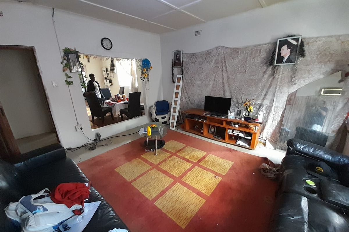 A living room area featuring a large wall opening connecting to an adjacent space, with visible ceiling and wall finish wear.