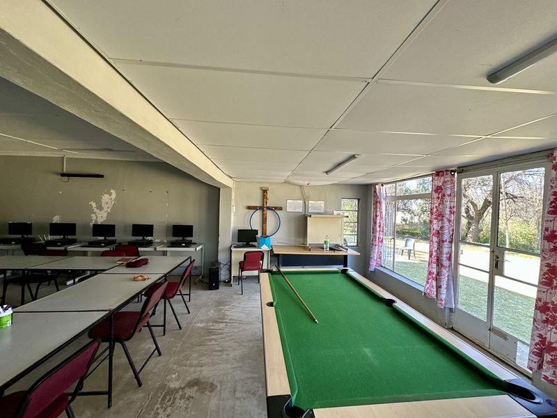 A multi-purpose utility space featuring concrete floors, suspended ceilings, and large glass doors leading to the garden, currently used as a study and recreation area.