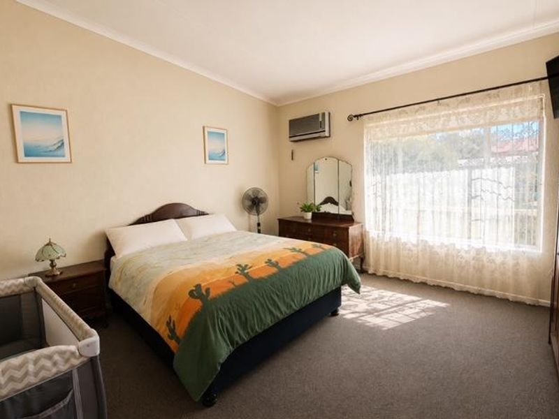 A spacious bedroom featuring carpeted flooring, a wall-mounted air conditioning unit, and large windows with curtains allowing natural light.