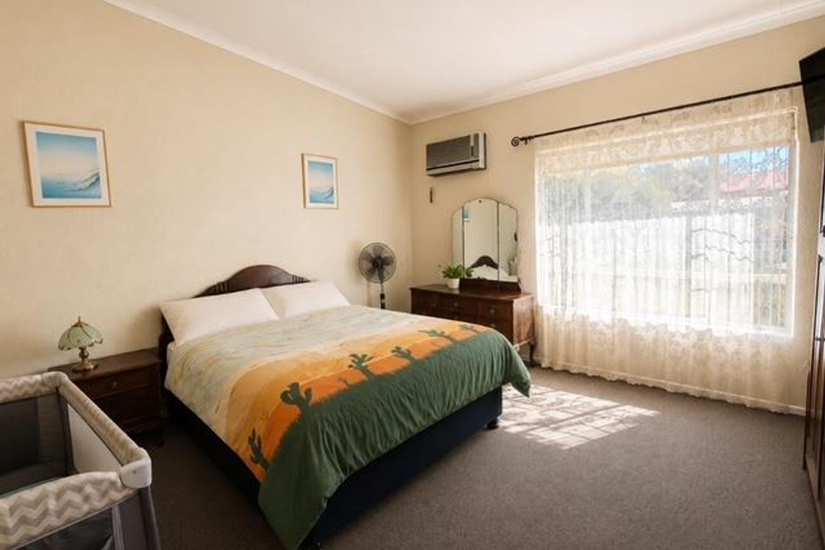 A spacious bedroom featuring carpeted flooring, a wall-mounted air conditioning unit, and large windows with curtains allowing natural light.