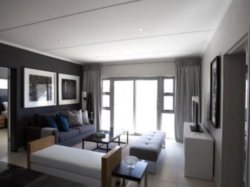 A modern, well-lit living room featuring tiled floors, recessed lighting, and large sliding glass doors that provide access to the outdoor area.