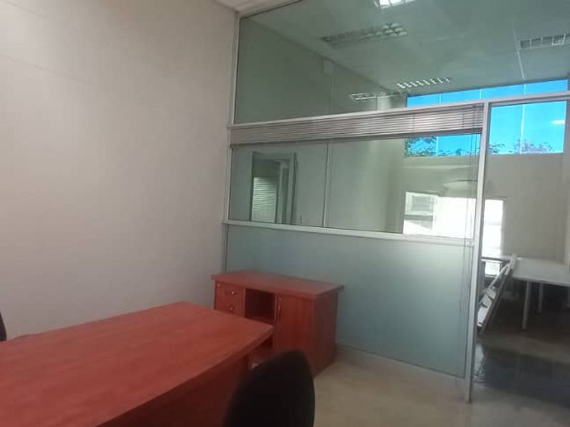 A professional office space featuring a glass partition wall, suspended ceiling, and recessed lighting, providing a bright and functional work environment.