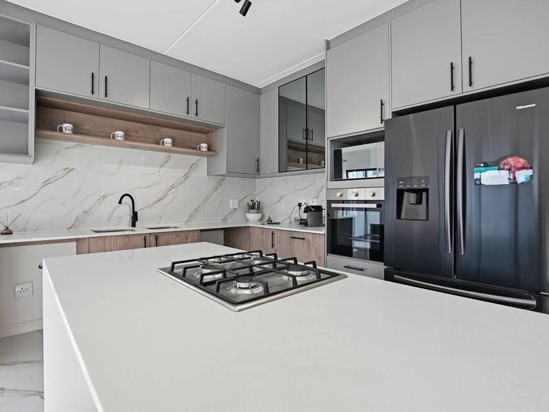 Modern kitchen featuring a central island with a gas hob, stone countertops, marble-look splashback, and integrated built-in appliances.