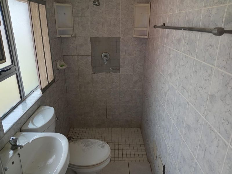 A compact bathroom featuring a shower, pedestal basin, and toilet with tiled finishes. The space requires maintenance and cosmetic updates to improve its condition.
